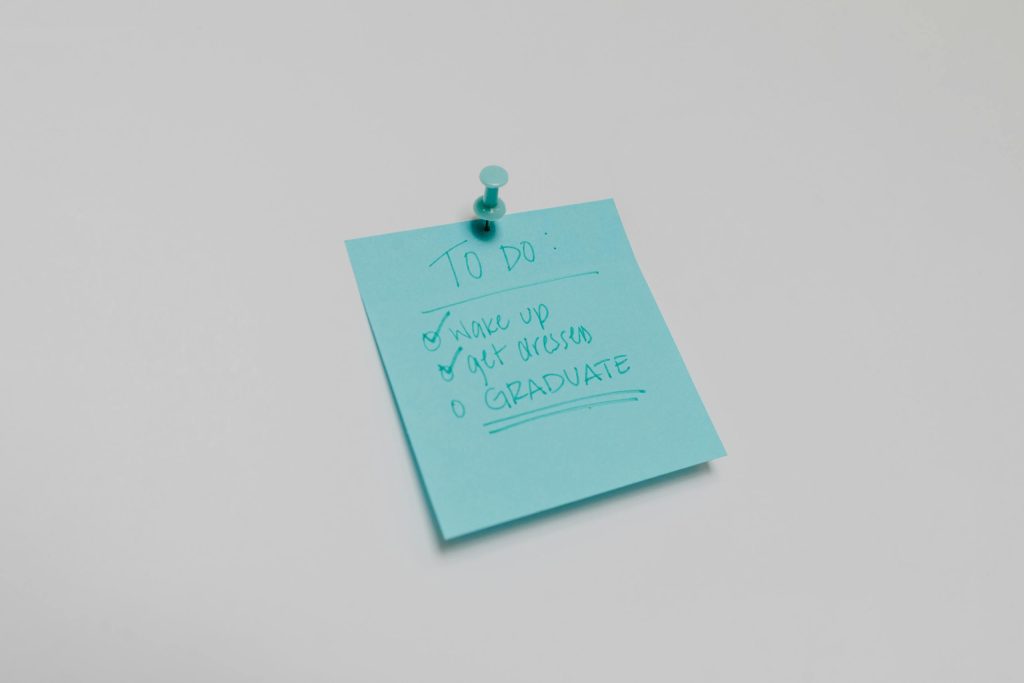A blue sticky note with a graduation to-do list pinned to a white surface.