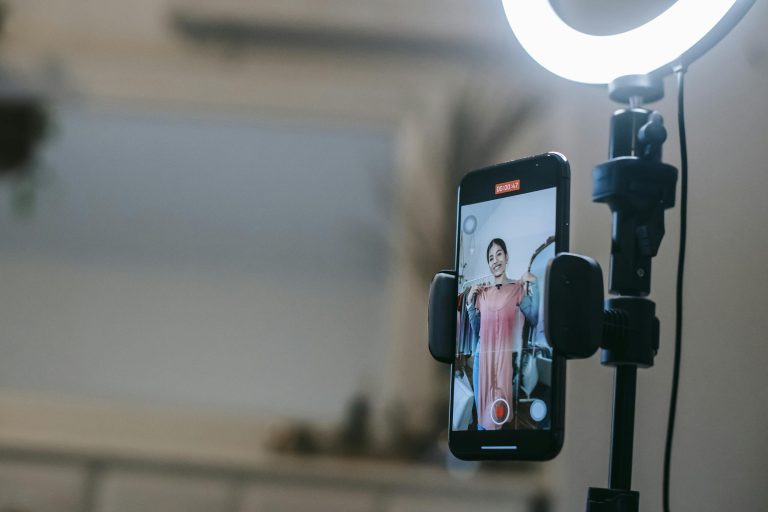 A woman livestreaming with a smartphone and ring light in a modern home setting.